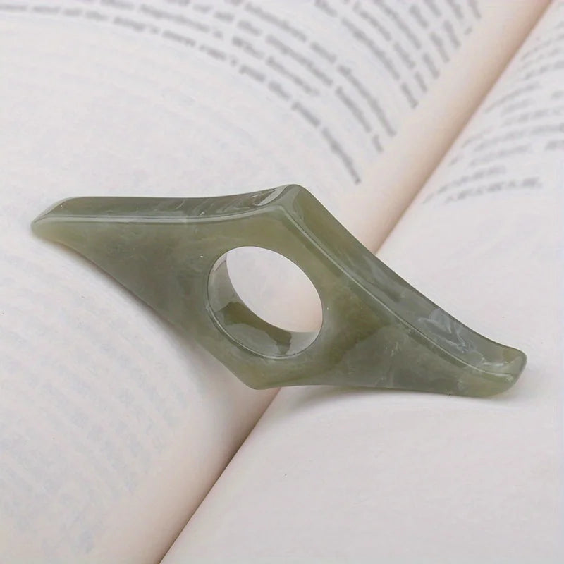 A translucent green resin thumb book stand with a cutout for holding a finger, resting on a white page.
