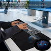 A hand is using a computer mouse on a black desk mat with a keyboard and monitor visible in the background.