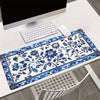 A blue and white floral patterned gaming mouse pad with a non-slip rubber base is displayed on a white desk.