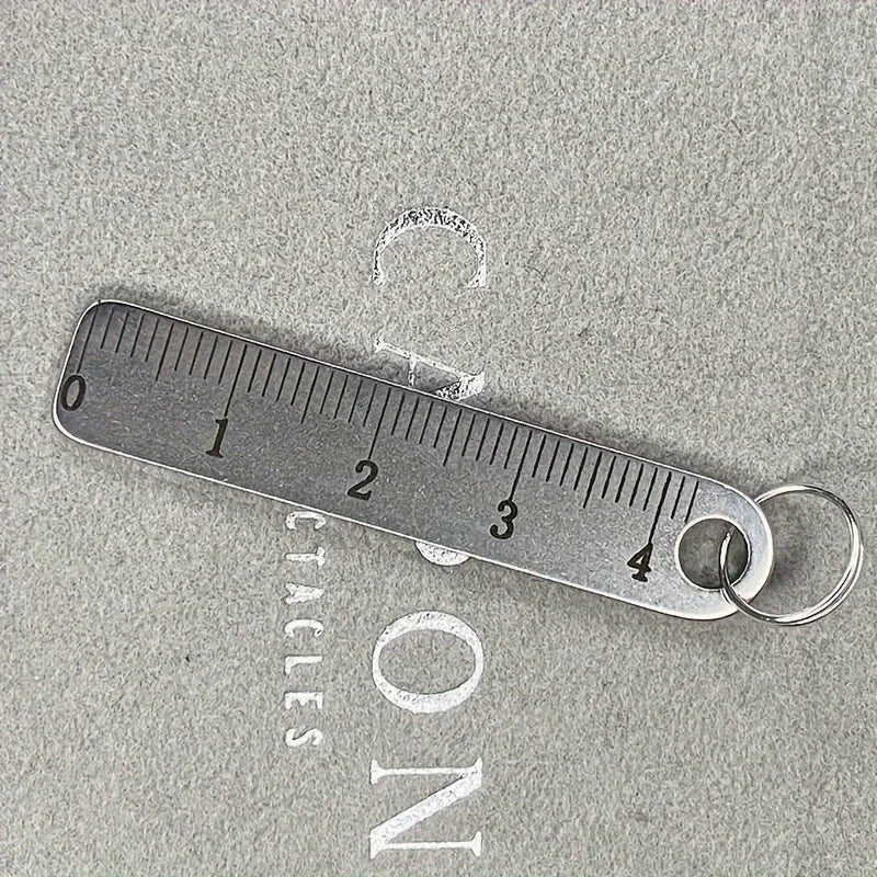 Stainless steel mini ruler keychain marked with centimeters and inches on a gray background.