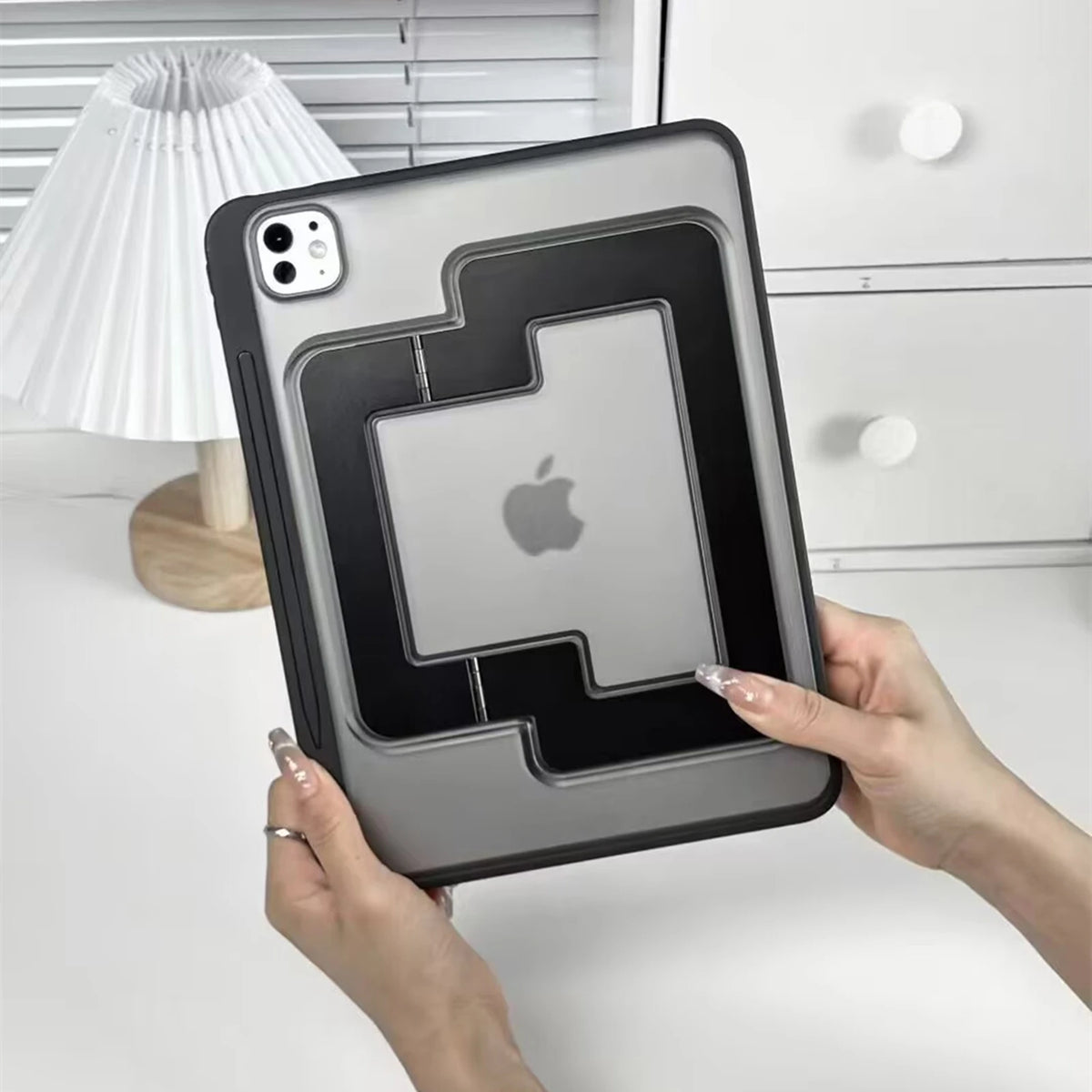 A hand holds a gray universal tablet and iPad protective case with a stand, featuring an Apple logo cutout.