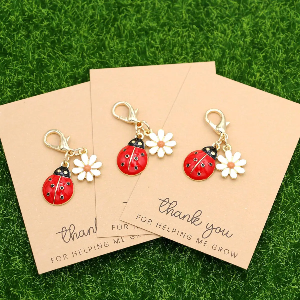A set of five cute ladybug and daisy keychains presented on kraft paper cards on green grass.
