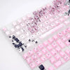 A close-up view of pink and black Raven Sakura theme PBT mechanical keycaps arranged in a translucent plastic tray.