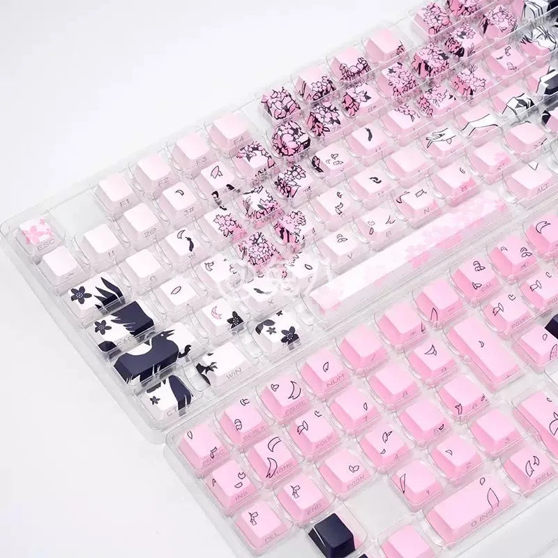 A close-up view of pink and black Raven Sakura theme PBT mechanical keycaps arranged in a translucent plastic tray.