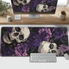 A dark purple and black desk mat featuring gothic skulls and roses, placed in front of a computer monitor and keyboard.