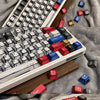 Nahaufnahme einer weißen mechanischen Tastatur mit individuellen roten und blauen Tastenkappen auf einer grauen Stoffoberfläc