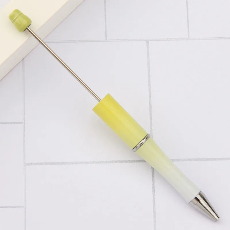 A yellow DIY beadable pen with a green cap resting on a white surface.