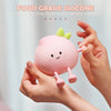 A hand holds a pink, peach-shaped silicone night light with a green leaf on top.