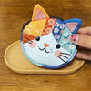 A patchwork cat face coin purse with a zipper featuring various fabric patches in orange, blue, and white.