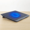 A black laptop cooling pad with a blue glowing fan is placed on a wooden surface.