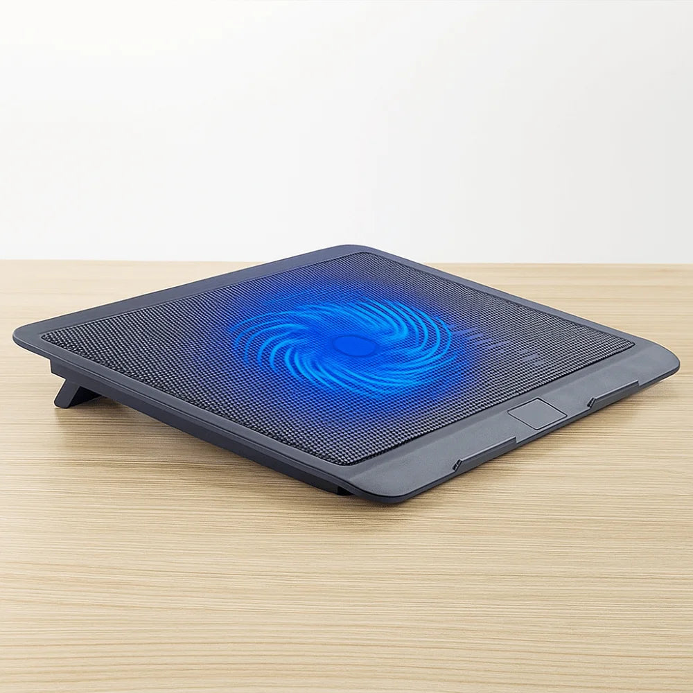 A black laptop cooling pad with a blue glowing fan is placed on a wooden surface.