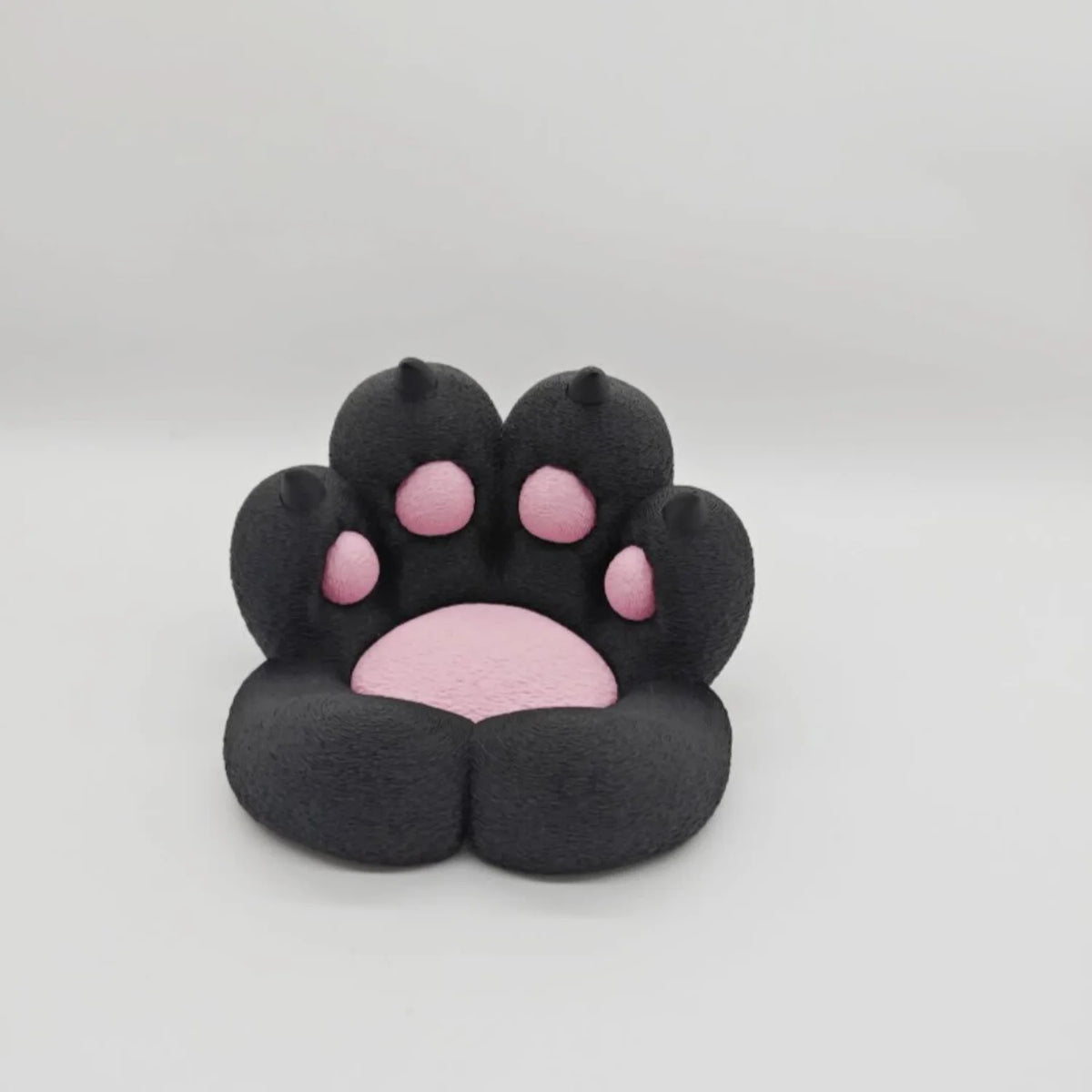A black 3D printed cat paw phone stand with an anti-slip base featuring pink details.