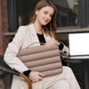 A woman holds a beige protective laptop sleeve bag with reinforced padding in an indoor setting.