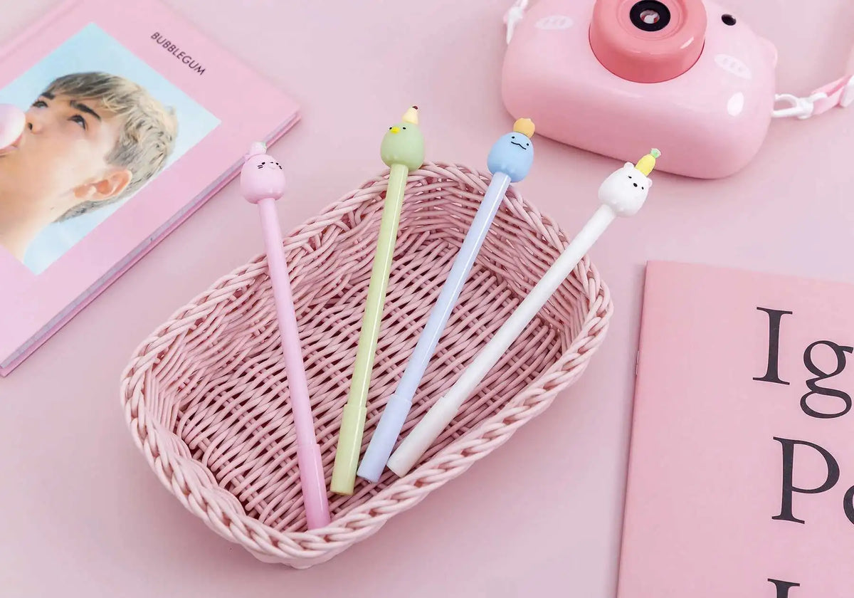 A pink woven basket holds several cute cartoon fruit gel pens in various pastel colors on a pink background.