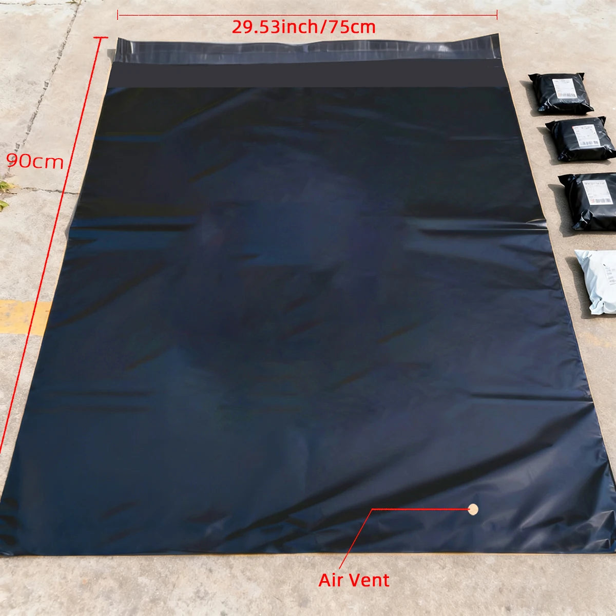 A black waterproof self-sealing shipping bag is laid flat on a concrete surface, showing its dimensions and an air vent.