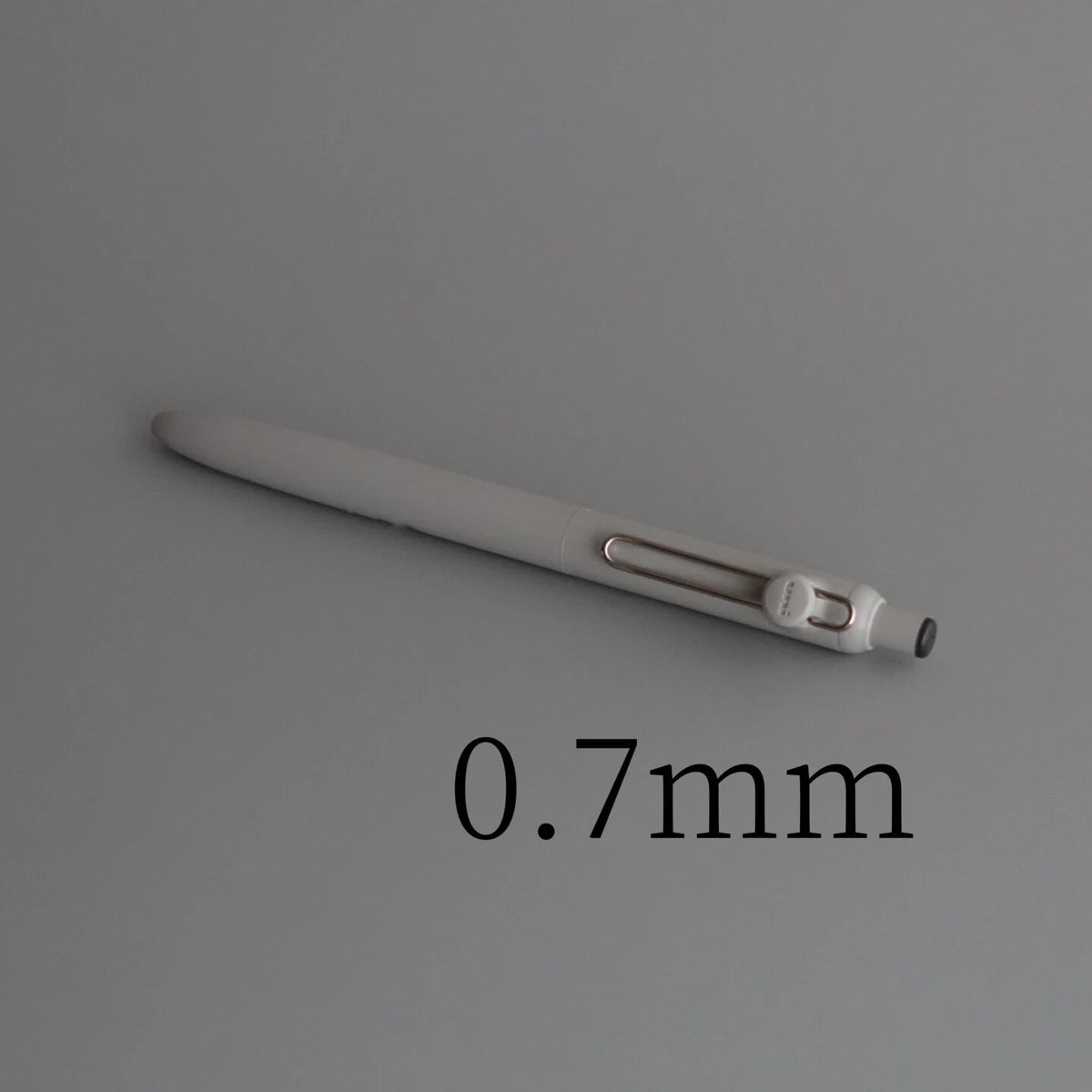 A close-up view of a silver precision gel pen with a 0.7mm tip resting on a gray surface.
