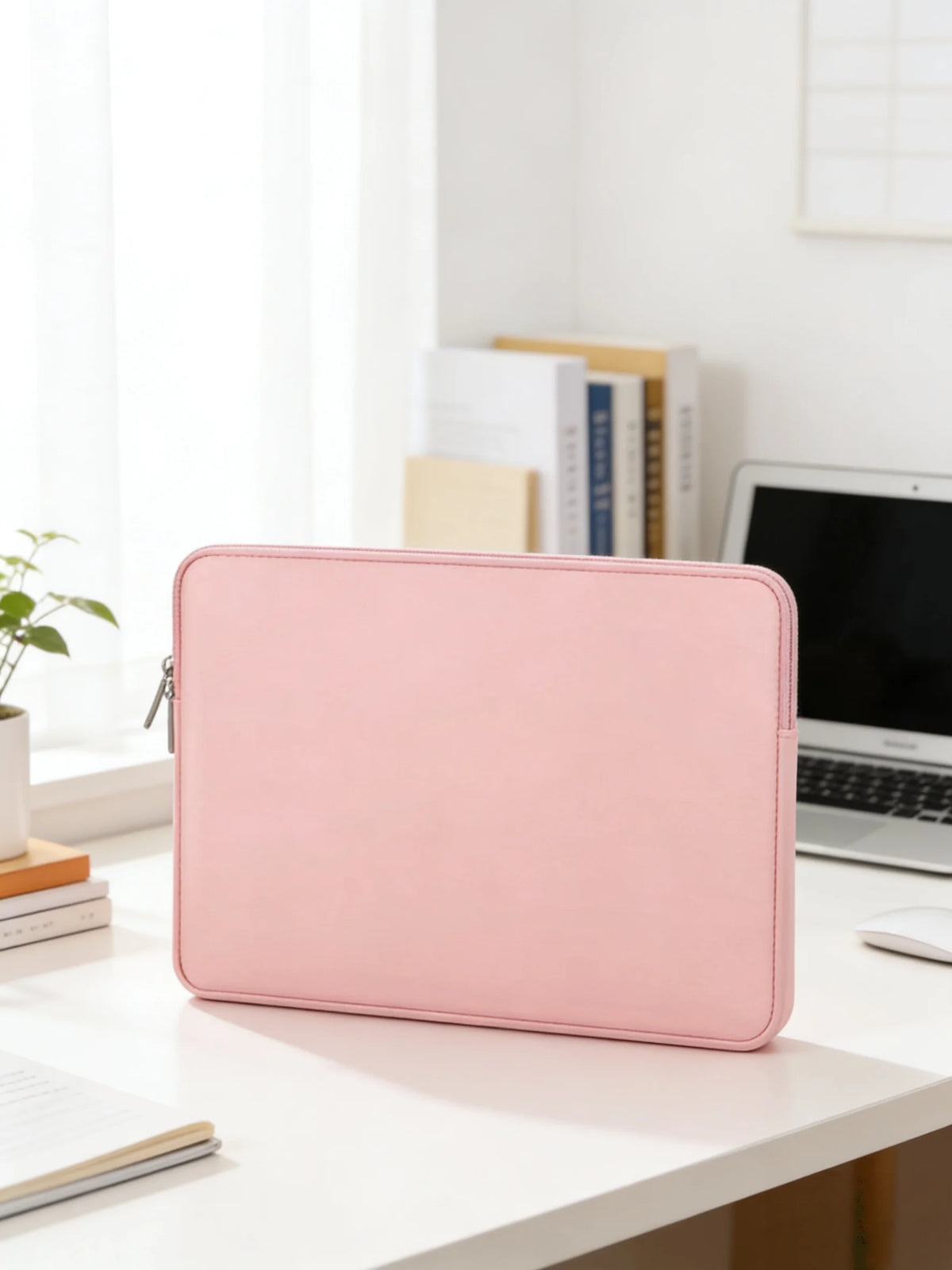 A pink waterproof PU leather laptop sleeve resting on a white desk next to a laptop and books.