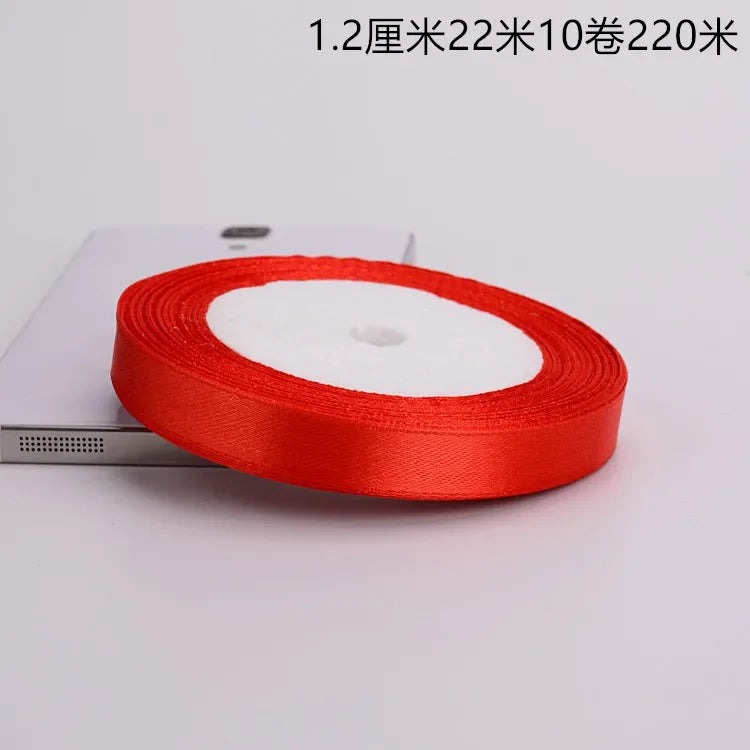 A roll of red satin ribbon with a white center core is shown on a white surface.