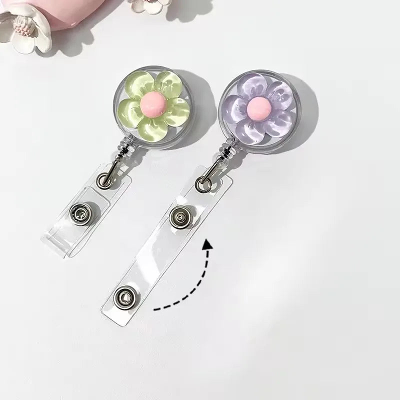 A pair of clear retractable ID badge holders with floral pull buckles, featuring light green and pink flowers.