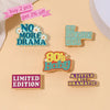 A set of enamel pins featuring phrases like No More Drama, Ever Sarcastic, 80s Baby, Limited Edition, and A Little Bit Dramat