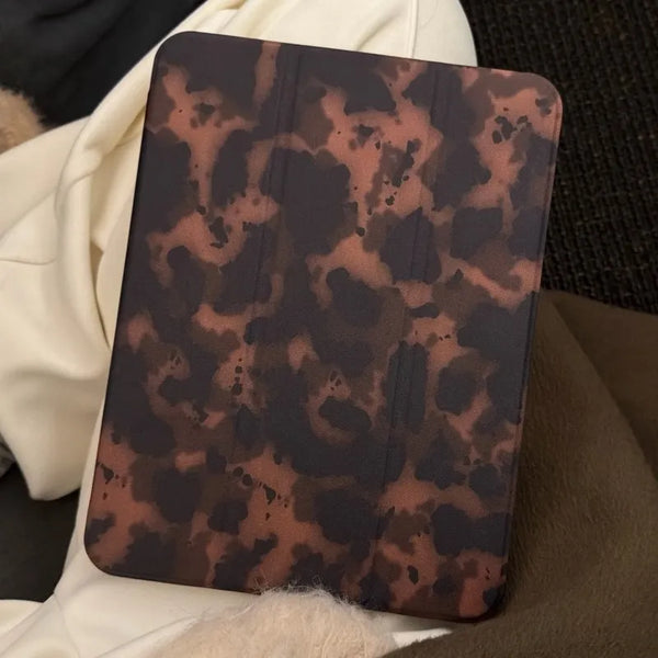 A dark brown leopard print leather tablet cover resting on a soft white blanket.