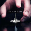 A hand holds a silver metal spinning top fidget toy against a dark background with the text The dream is real.