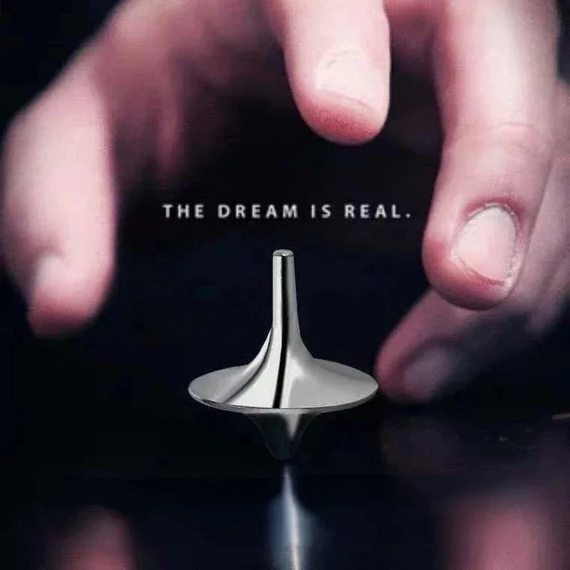A hand holds a silver metal spinning top fidget toy against a dark background with the text The dream is real.
