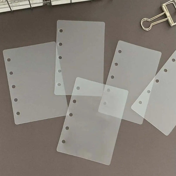 A set of ten transparent divider pages for loose-leaf planners, lying on a gray surface.