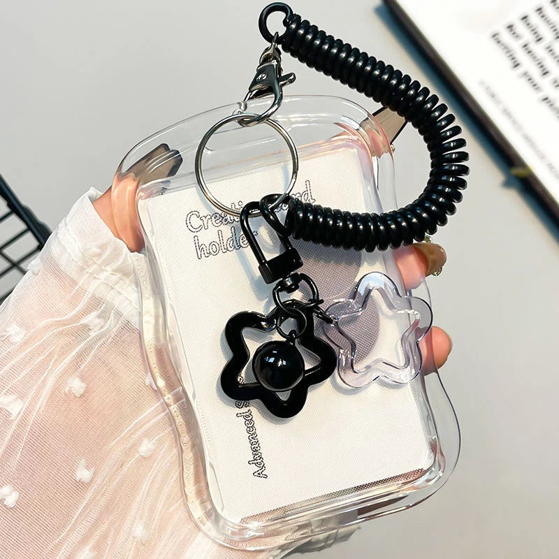 A clear card holder with a black keychain featuring a star charm and a round pendant.