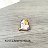 Un pequeño broche de esmalte con la cara de un gato naranja y blanco tierno sobre una superficie de madera.