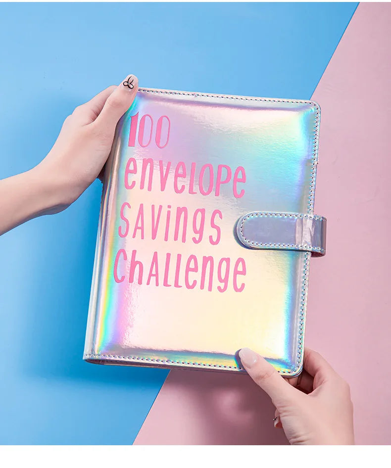 Eine Hand hält einen glänzenden rosa Umschlag mit der Aufschrift "100 Envelope Savings Challenge" vor einem blau-rosa Hinterg