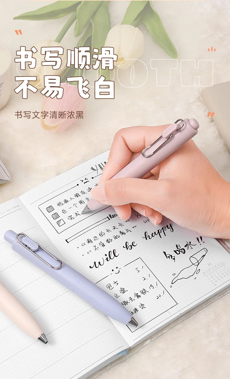 A hand writes on a notebook using a light purple Uni-Ball One Mini Cute Gel Pen with rich, quick-dry ink.