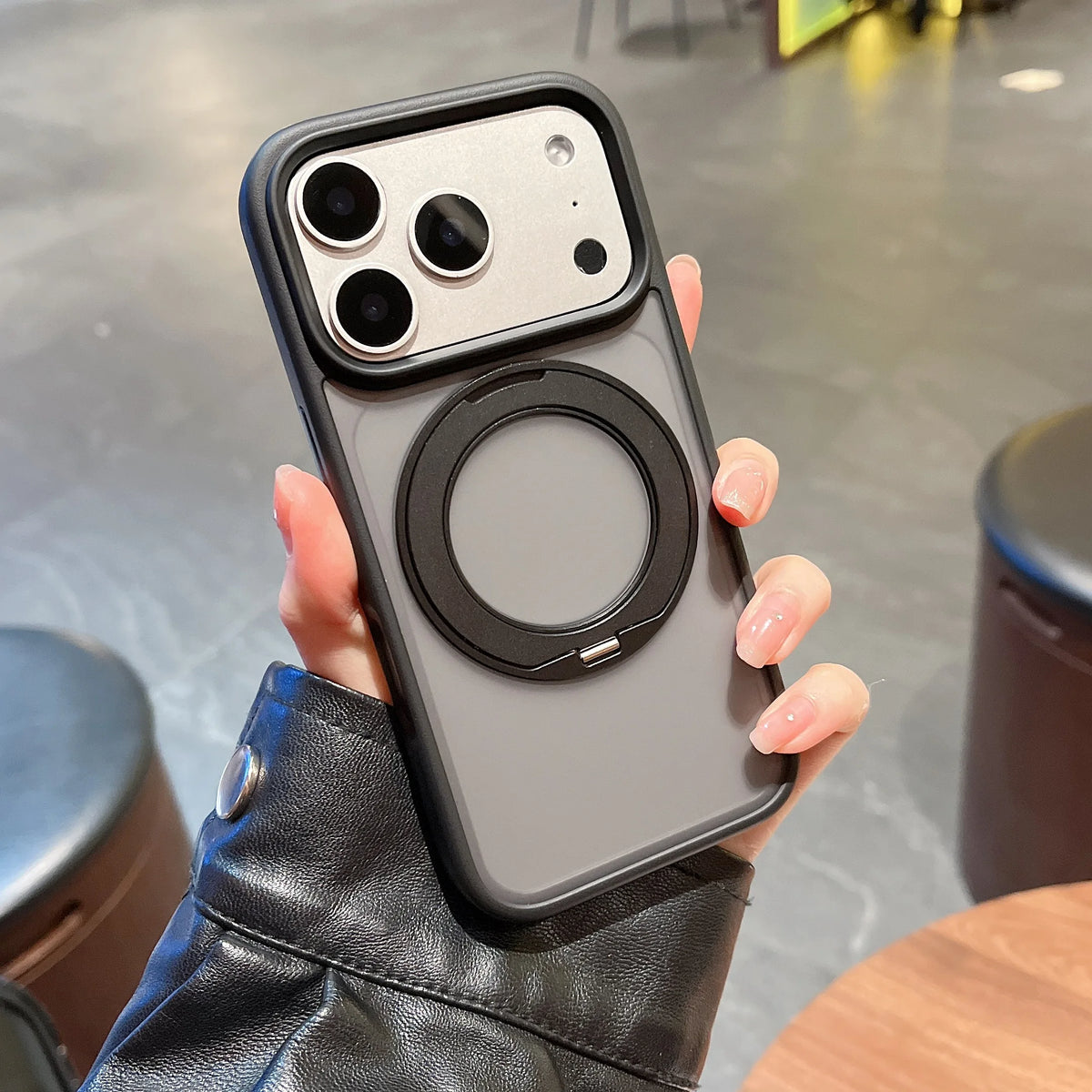 A hand holds a gray magnetic phone case with a rotating stand, showing the back and camera module.