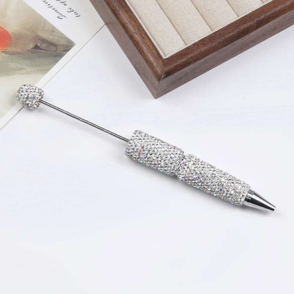 A silver pen accessory featuring a rhinestone ball on the tip and a sparkly, textured body.