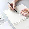 A hand is using a black pen to mark a transparent ruler on a white notebook page.