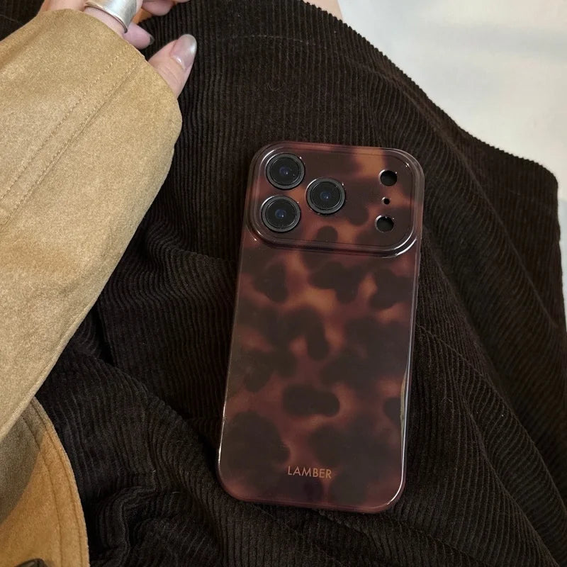 A brown leopard print phone case is shown resting on a dark green sweater, held by a hand.