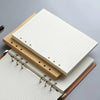Una pila de resmas de cuadernos sin hojas y un cuaderno encuadernado en espiral sobre una superficie gris.