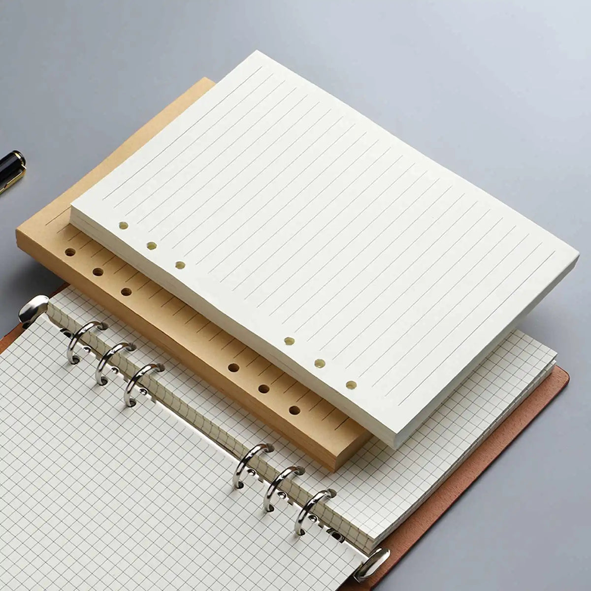 Una pila de resmas de cuadernos sin hojas y un cuaderno encuadernado en espiral sobre una superficie gris.