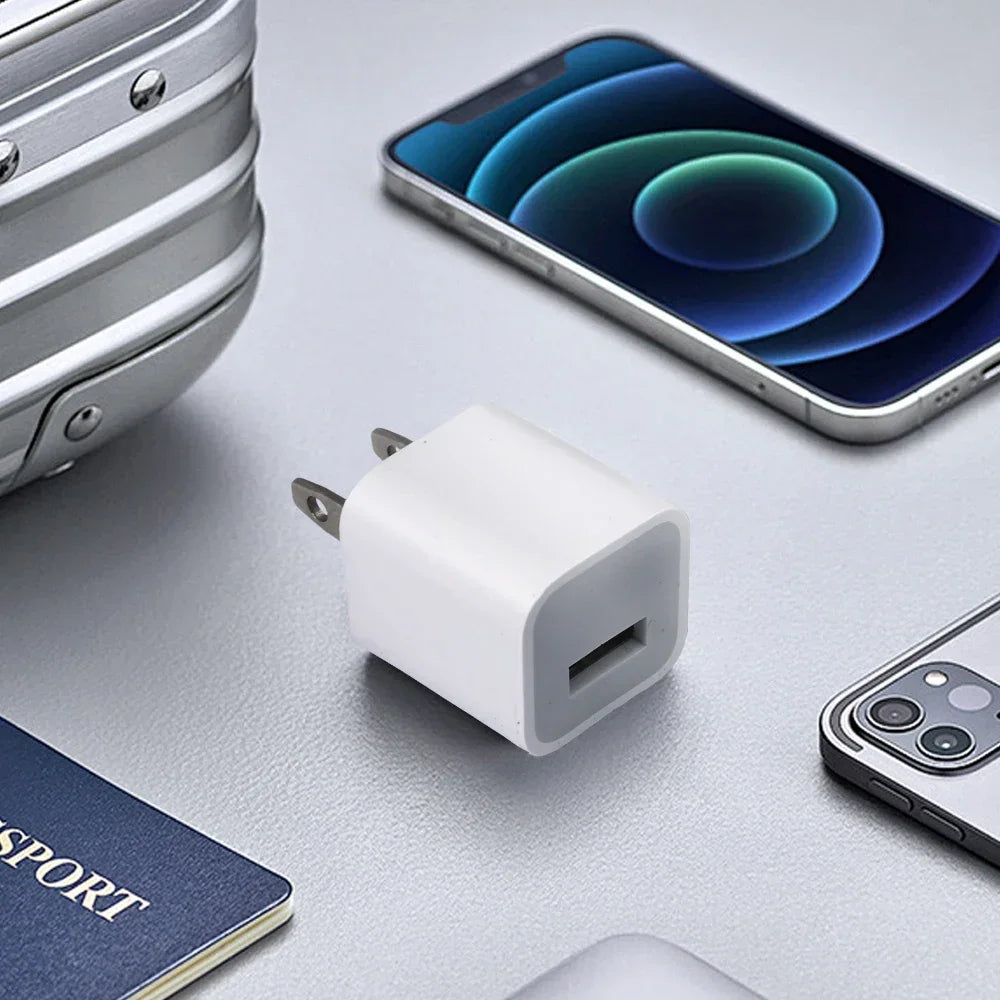 A white universal USB wall charger cube is shown next to a smartphone and a notebook on a light gray surface.