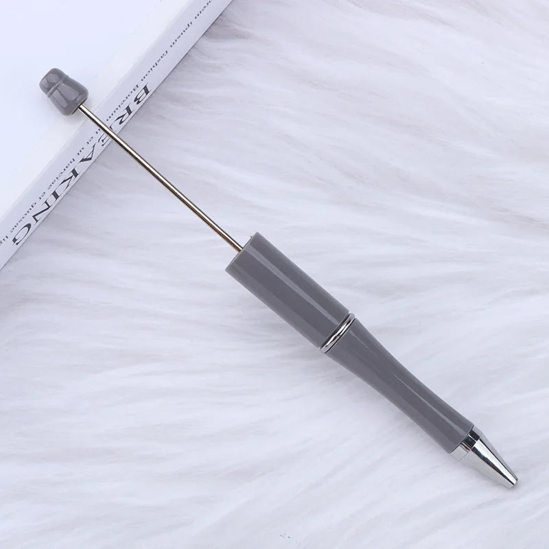 A silver DIY beadable pen with a purple tip rests on a white surface.