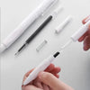 A hand holds a white and black smooth writing gel pen with a silver spring mechanism and several pens on a white surface.