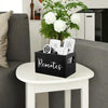 A black storage box with dividers holding various remote controls and small electronic devices on a white table.