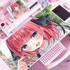 A close-up of an anime-style illustration featuring a pink-haired girl, with various office supplies and a computer tablet in