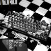 A close-up of a black mechanical keyboard with PBT keycaps, set against a black and white checkered background.