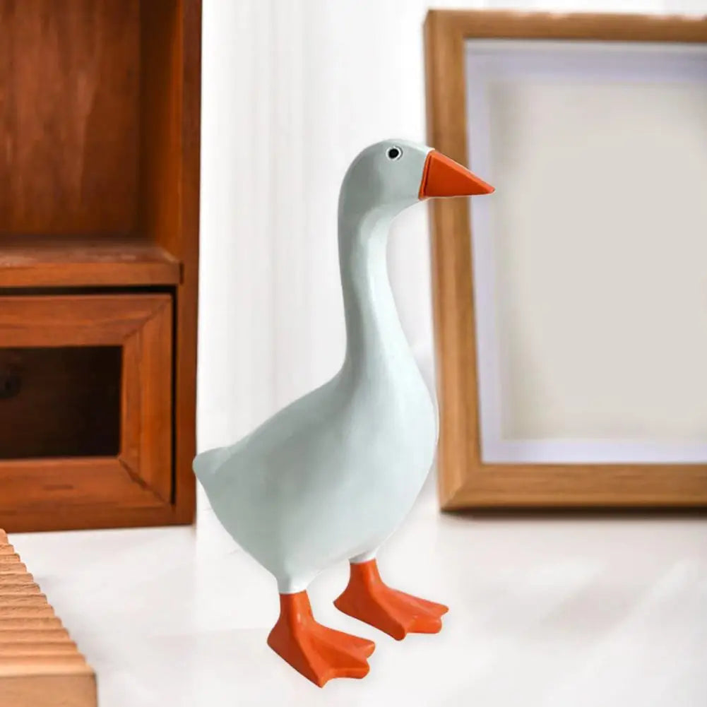 A small, light blue resin duck figurine with an orange beak and feet sitting on a white surface.