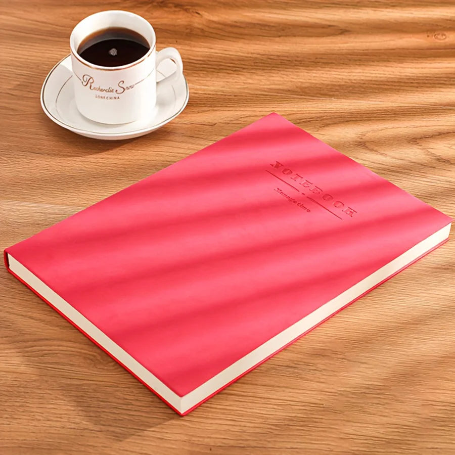 A red notebook titled VOETBOOK is placed next to a white cup and saucer on a wooden surface.