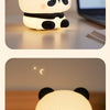 A white and black panda silicone night light with touch control sitting on a wooden surface.