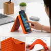 An orange flexible silicone multi-angle stand is shown supporting a smartphone on a white desk.