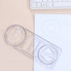 A clear plastic geometric drawing ruler with rotating angles is shown on a white background next to a keyboard.