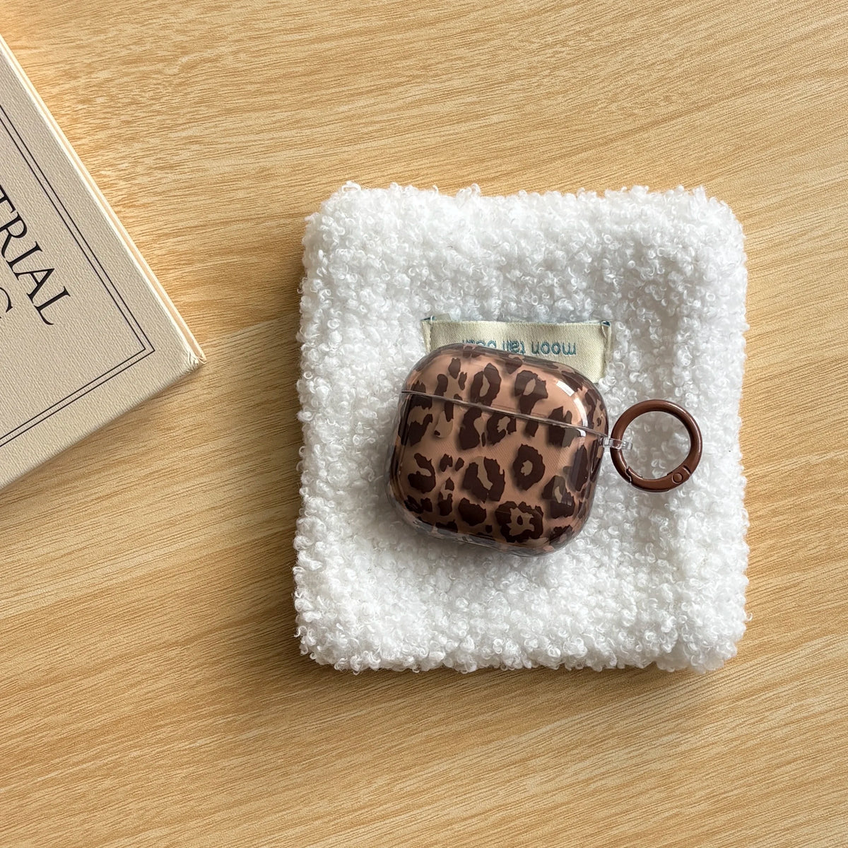 A leopard print earphone case cover rests on a white fluffy towel on a wooden surface.